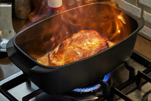 Stück Rindfleisch gebraten mit Zwiebeln in Weinsoße in rechteckiger Pfanne auf Gasherdfeuer Flombe Französische Gourmetküche