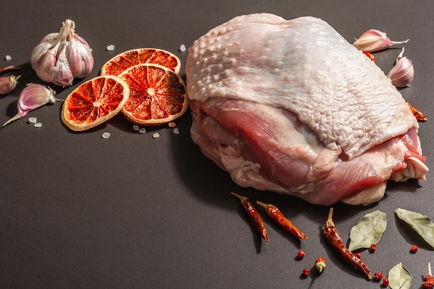 Stück rohes Putenfleisch mit Gewürzen. Eine nützliche Zutat für die Zubereitung gesunder Lebensmittel, Gewürze, Knoblauch. Modernes hartes Licht, dunkler Schatten, Betonhintergrund aus schwarzem Stein, Kopierraum