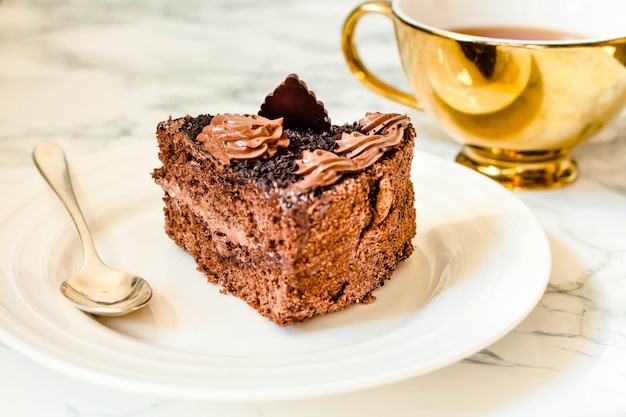 Stück Schokoladenkuchen in einem weißen Teller und einer goldenen Tasse Kaffee, Nahaufnahme. Selektiver Fokus. Saison- und Feiertagsmuster