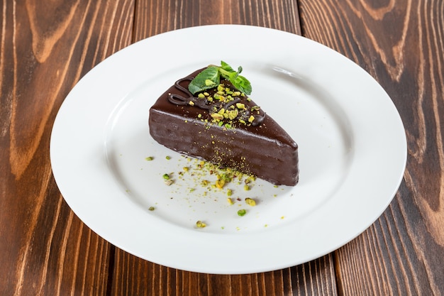 Stück Schokoladenkuchen mit Pistazien und Minzblättern auf weißem Teller