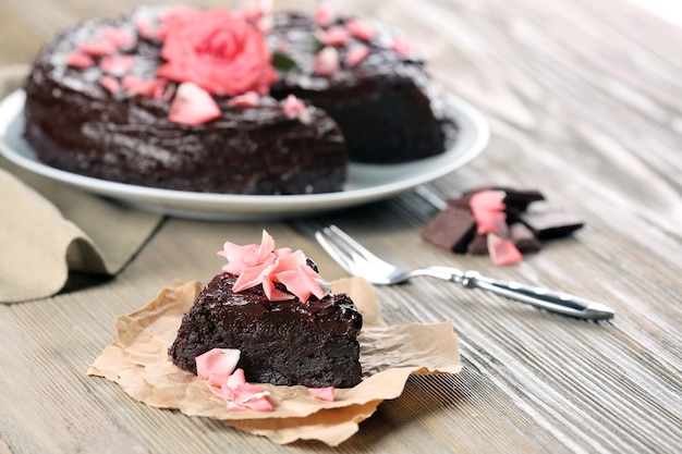 Stück Schokoladenkuchen verziert mit Blumen auf braunem Holztisch