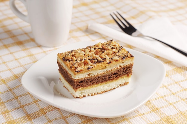 Stück süßer Kuchen mit Nüssen und weißer Tasse auf dem Tisch