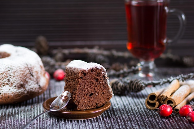 Stück weihnachtsschokoladenbiskuit mit zuckerpulver auf dem holztisch mit glas rotem tee und zimtstangen