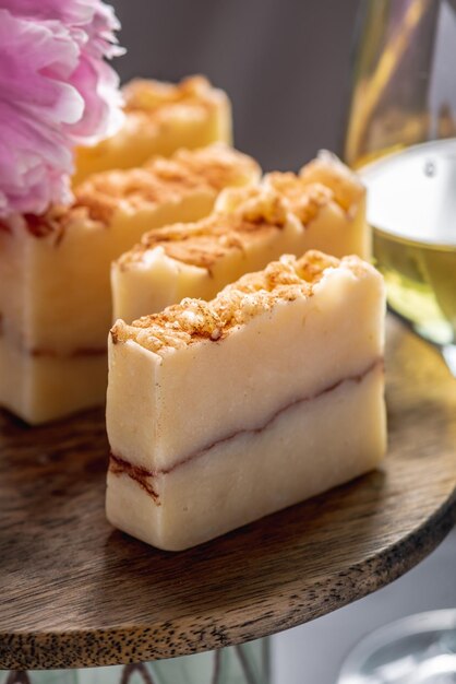 Stückchen natürliche Seife auf einem Holzstand umgeben von Blumen und einem Glas Wein Konzept organischer Kosmetika für die Hautpflege eine schöne Postkarte ein ungewöhnliches Produkt eine interessante Idee