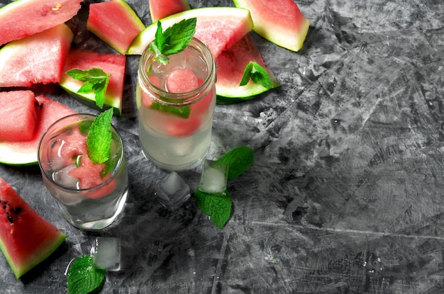 Stücke der Wassermelone Geschnittenes saftiges Wassermelonen- und Wassermelonencocktail mit Minze auf einer grauen Betonoberfläche