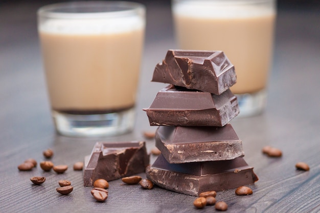 Stücke dunkler Schokolade, Kaffeebohnen und Tassen Kakao oder Kaffee mit Milch auf Holztisch.