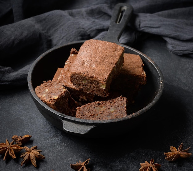 Stücke gebackener Brownie in einer schwarzen Bratpfanne aus Metall auf dem Tisch