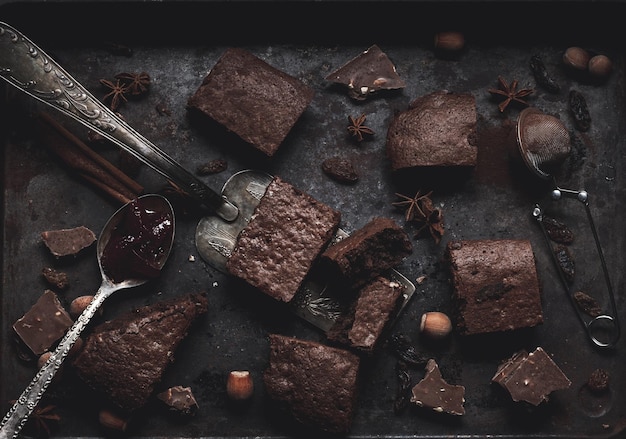 Stücke gebackener Schokoladen-Brownie-Torte in einem Metallbackblech auf einem schwarzen Tisch, Ansicht von oben