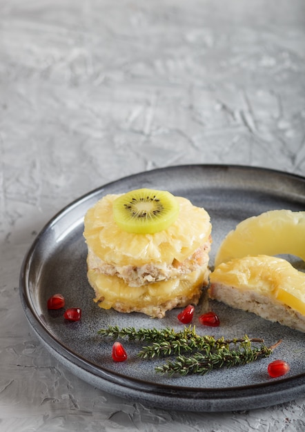 Stücke gebackenes Schweinefleisch mit Ananas, Käse und Kiwi auf grauer Platte.