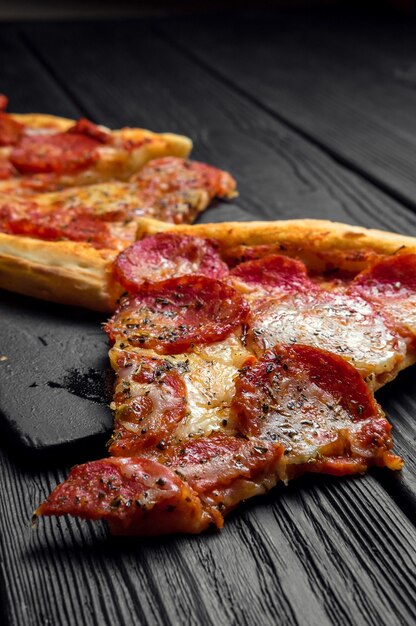 Stücke Pizza Peperoni auf dunkelschwarzem Holzbrett, traditionelle italienische Pizza