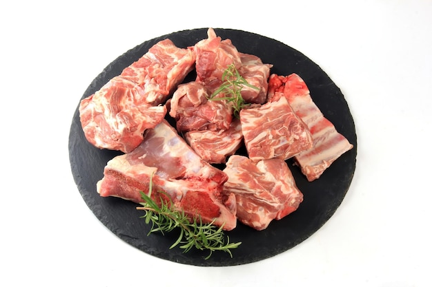 Stücke rohes Fleisch auf einer runden schwarzen Steinplatte auf weißem Hintergrund, frisches Fleisch mit Knochen