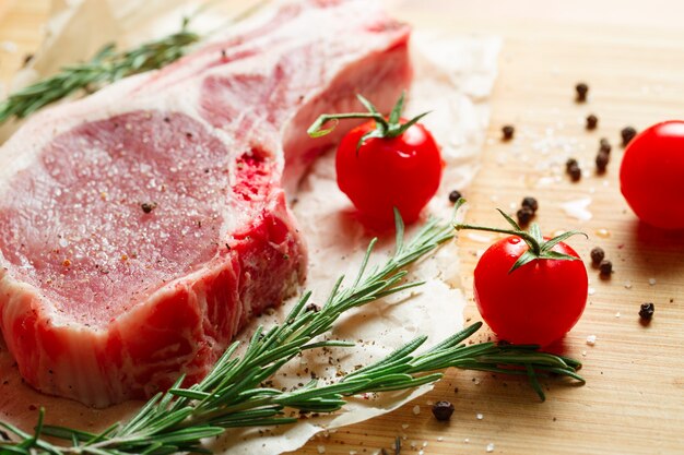 Stücke rohes Fleisch mit Rosmarin und Tomaten.