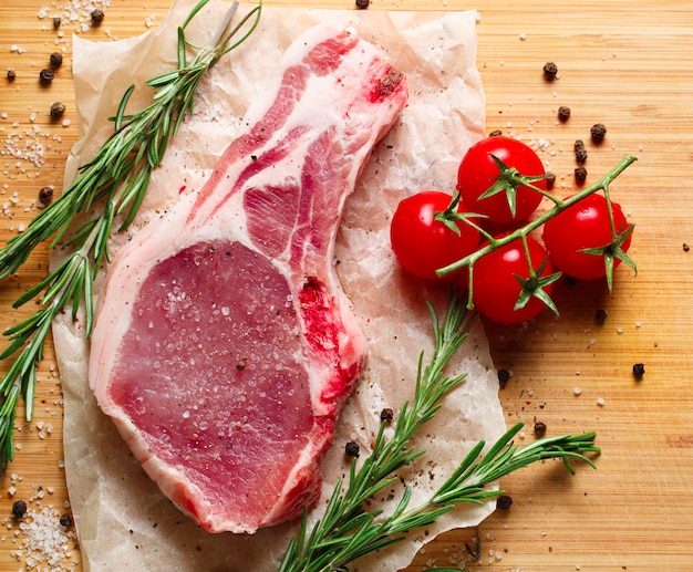 Stücke rohes Fleisch mit Rosmarin und Tomaten.