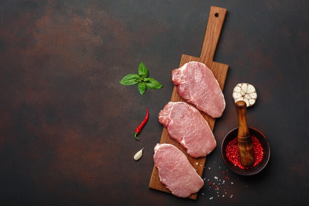 Stücke rohes Schweinefleischsteak mit Basilikum, Knoblauch, Pfeffer, Salz und Gewürzmörtel auf Schneidebrett