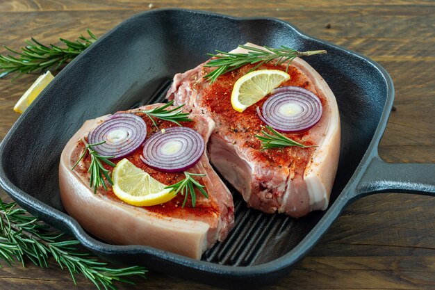 Stücke rohes Schweinesteak mit Gewürzen und Kräutern Rosmarin, Salz und Pfeffer auf Holzbrett auf Holzhintergrund im rustikalen Stil.