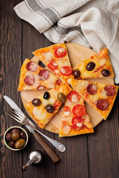 Stücke verschiedener griechischer Pizzen mit Oliven, italienischer Margarita und Pepperoni auf einem dunklen Holz rustikal.