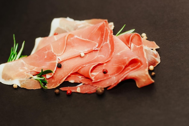 Stücke von getrocknetem Schweinefleisch Jamon Prosciutto auf einem schwarzen Brett