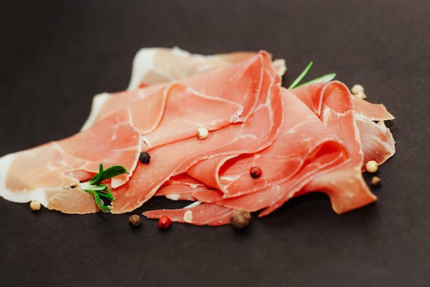 Stücke von getrocknetem Schweinefleisch Jamon Prosciutto auf einem schwarzen Brett