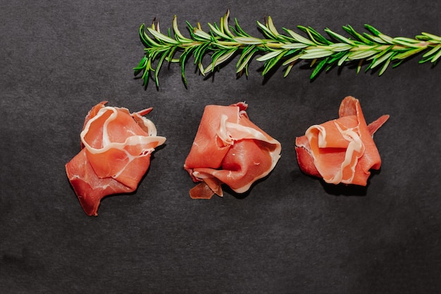 Stücke von getrocknetem Schweinefleisch Jamon Prosciutto mit Rosmarin auf einem schwarzen Brett
