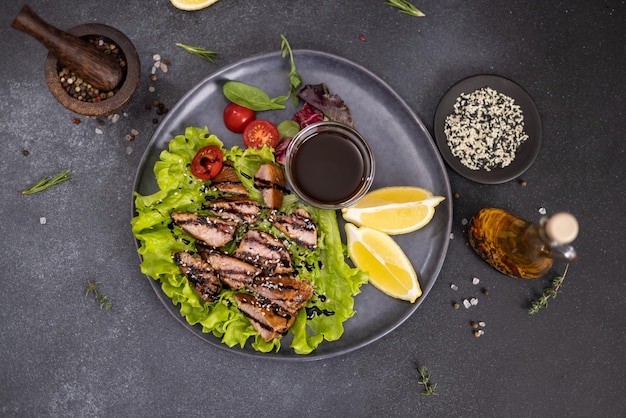 Stücke von organischem gegrilltem Thunfischsteak auf einem schwarzen Keramikgericht mit Salat auf einem Tisch