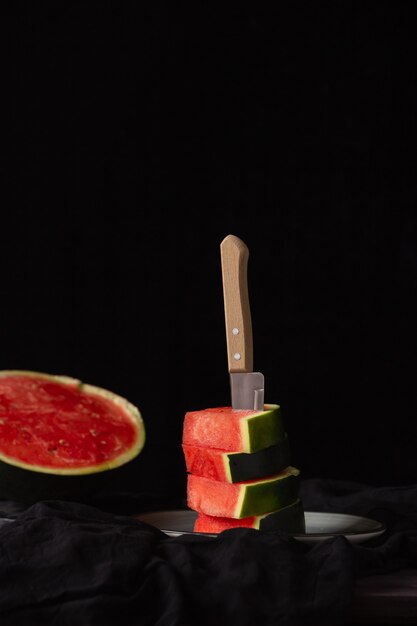 Stücke Wassermelone auf schwarzem Hintergrund und ein Messer. Rustikaler Stil.