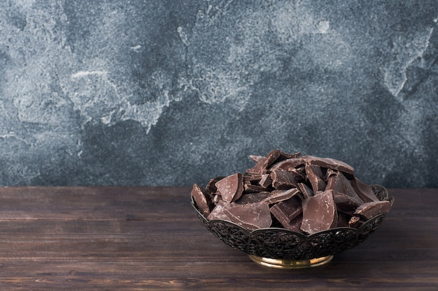 Stücke zerquetschte dunkle Schokolade in einer Platte auf einem dunklen Hintergrund.
