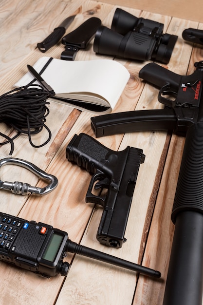 Sturmgewehr, Pistole, Messer mit Scheide, Kompass und Notizbuch mit Stift auf Tabelle.