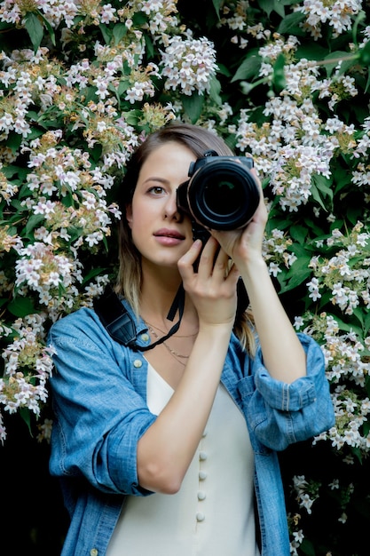 Style Frau mit Kamera in der Nähe eines blühenden Baumes in einem Garten im Frühling