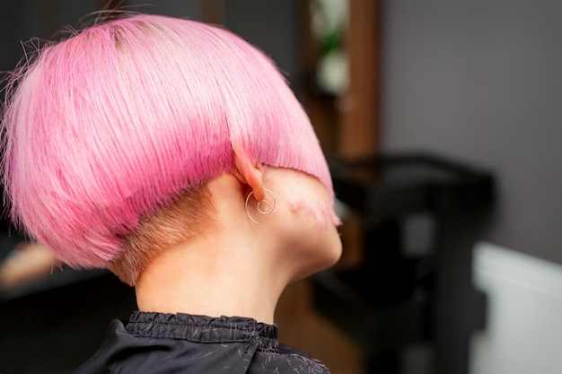Styling und Schneiden von gefärbtem rosa Haar des jungen Models in der Rückansicht in einem Friseursalon. Rosa kurze Frisur.