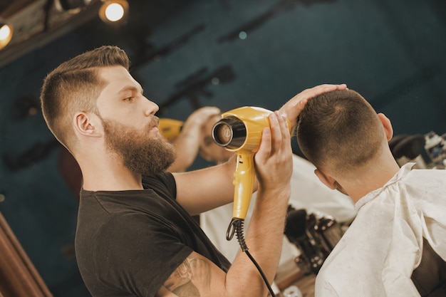 Styling vom Profi. Porträt eines Friseurs, der das Haar seines Kunden anredet es unter Verwendung eines Haartrockners trocknet