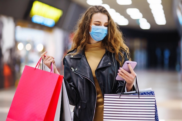 Stylische Frau in medizinischer Schutzmaske mit Einkaufstüten mit ihrem Telefon Modestil