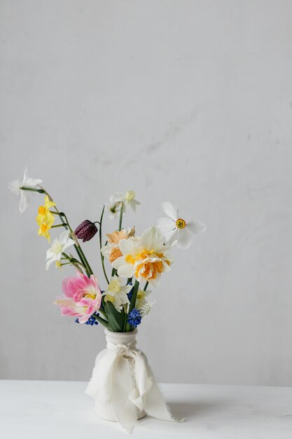Stylische Frühlingsblumen in einer Vase mit Band auf einem rustikalen weißen Tisch Glücklichen Frauentag und
