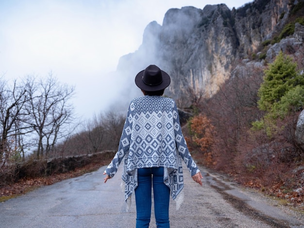 Stylische Hipster-Frau mit Hut, die eine Bergstraße hinuntergeht