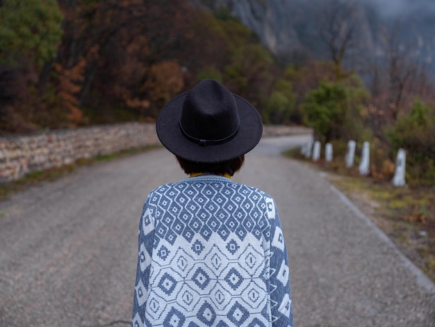 Stylische Hipster-Frau mit Hut, die eine Bergstraße hinuntergeht