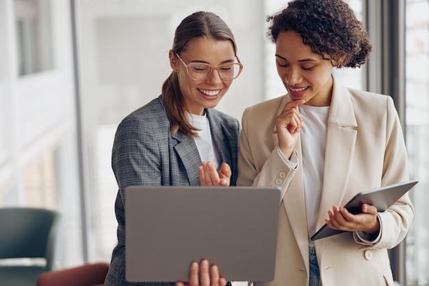 Stylische Managerinnen stehen in einem modernen Büro und arbeiten mit Laptop und digitalem Tablet