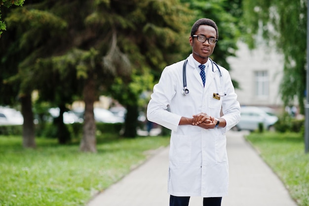 Stylischer afrikanisch-amerikanischer Arzt mit Stethoskop und Laborkittel an Brille im Freien gestellt