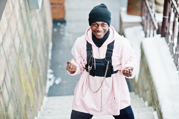 Stylischer afroamerikanischer Mann im urbanen Stil in rosafarbenem Hoodie, der am Wintertag und Boxhänden posiert