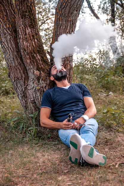Stylischer bärtiger Mann dampft und setzt eine Dampfwolke frei Die Zigarette mit neuer Technologie
