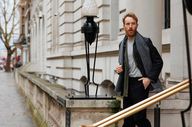 Stylischer bärtiger Mann in Jacke und Schal steigt die Treppe hinunter und verlässt das Gebäude