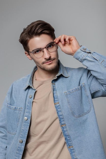 Stylischer, gutaussehender Hipster-Profi in modischer Denim-Kleidung mit Hemd, Vintage-Brille und Blick auf die Kamera im Studio