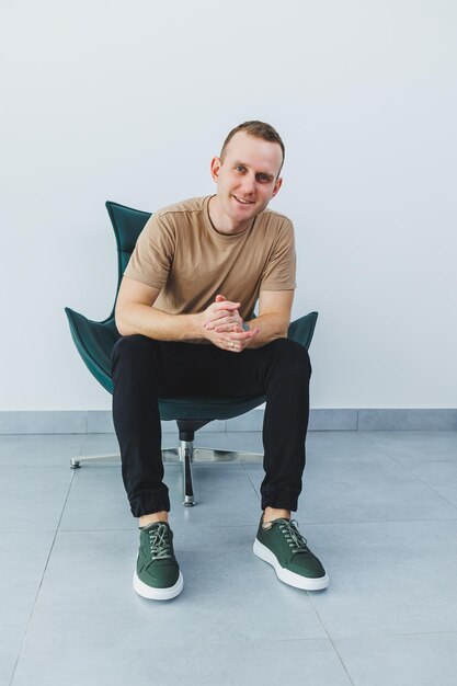 Stylischer junger Mann in einem beigen T-Shirt und einer schwarzen Hose, ein Mann in grünen Leder-Casual-Turnschuhen