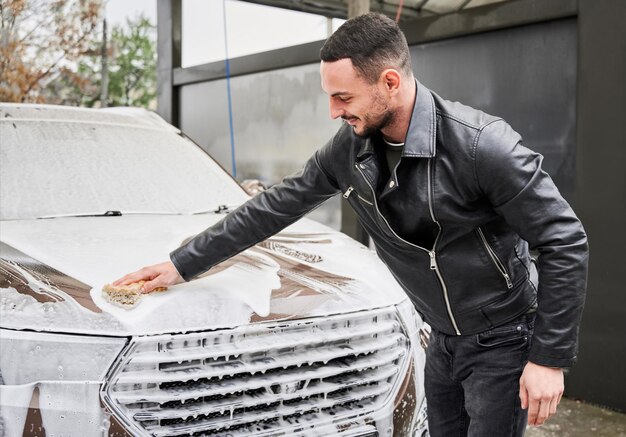 Foto stylischer kerl, der auto auf autowaschanlage im freien einseift