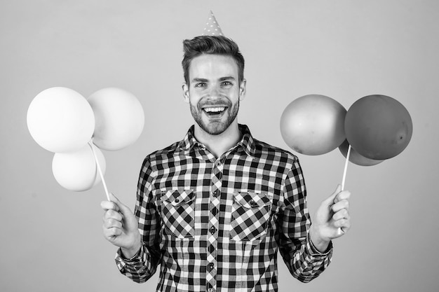 Foto stylischer typ mit trendiger frisur trägt kariertes hemd und hält partyballons im urlaub