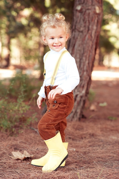 Stylisches Mädchen im Alter von 4-5 Jahren trägt Herbstkleidung und Gummistiefel im Park