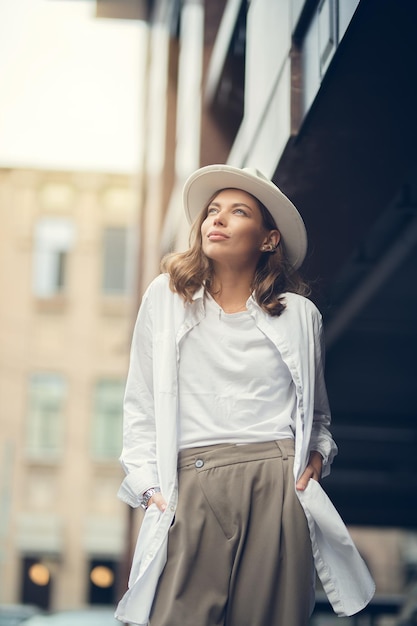 Stylisches Mädchen in weißer Hose und weißer Baumwollbluse posiert an der Wand