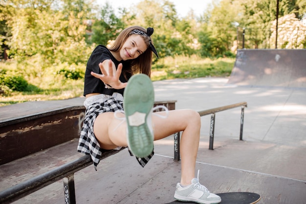 Stylisches Teenager-Mädchen mit Skateboard sitzend und chillend im Skaterpark