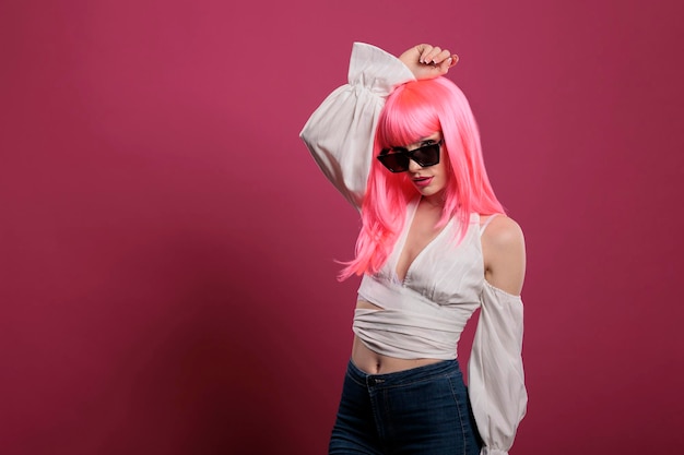 Stylisches weibliches Model mit trendiger Sonnenbrille vor der Kamera, das sich selbstbewusst und attraktiv vor rosa Hintergrund fühlt. Sinnliches hübsches Mädchen mit süßer Brille im Gesicht, funky Frisur.