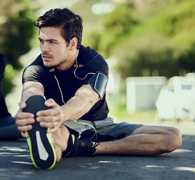 Su calentamiento es clave para su entrenamiento Toma de cuerpo entero de un apuesto joven calentando al aire libre antes de un entrenamiento