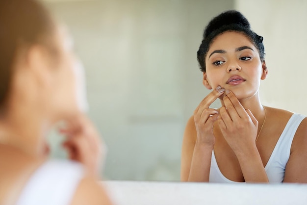 Su cambio de imagen matutino Fotografía de una mujer joven inspeccionándose la piel frente al espejo del baño