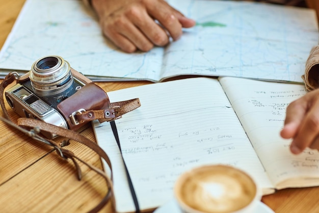 Su diario de viaje lo mantiene encaminado Fotografía de un turista no identificable mirando mapas y diarios de viaje mientras disfruta de un café en una cafetería